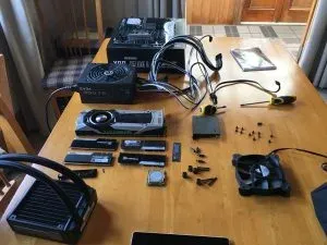 Every part laid out on a wooden dining table: power supply, board, graphics card, RAM, fan, cooler, screws and tools