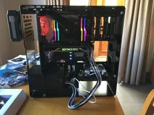 The built machine powered up on a table, rainbow-lit RAM, a green GEFORCE GTX logo and white cables looping out the front