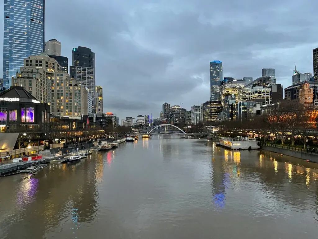The Yarra at dusk under heavy cloud, Southgate and the city towers lit, boats moored along the bank