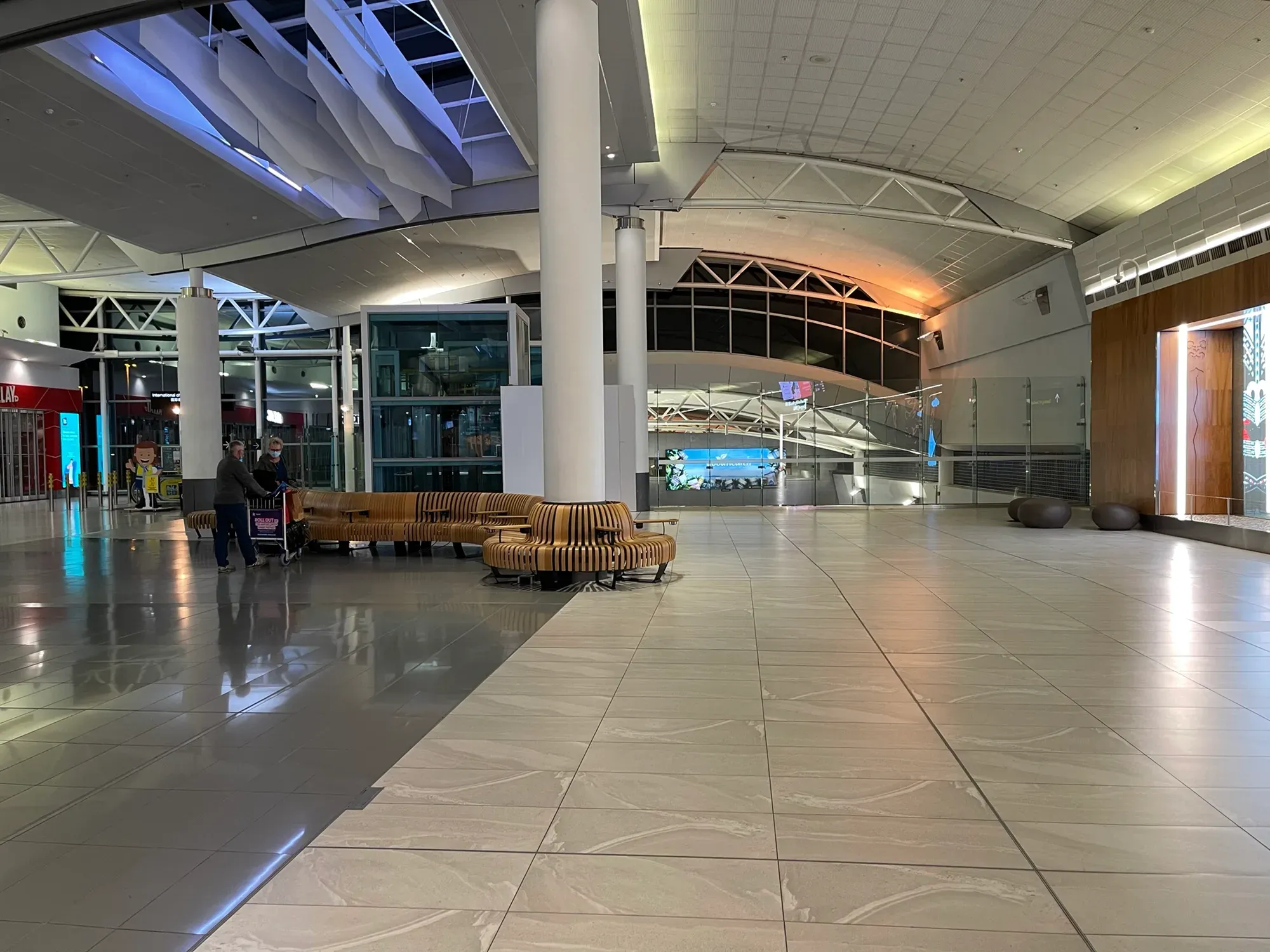 Two travellers with a luggage trolley alone in a vast tiled concourse