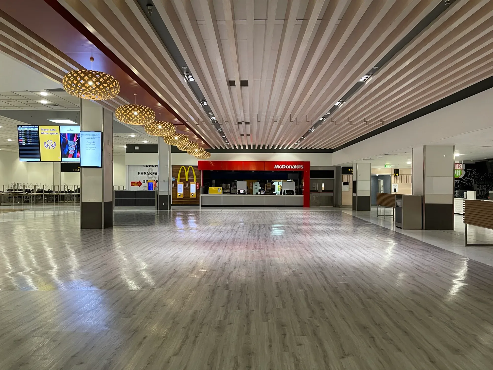 A deserted departures hall, the McDonald's counter dark and a screen reading "Travel safe. Allow space."