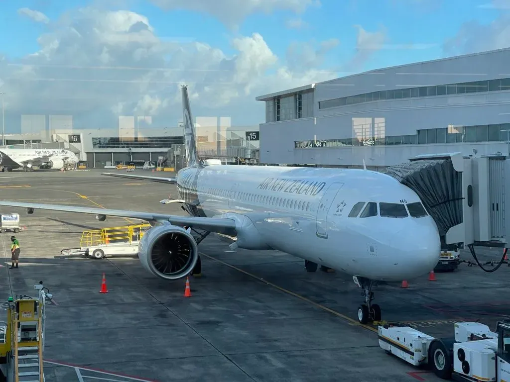 An Air New Zealand jet parked at the gate with the airbridge attached