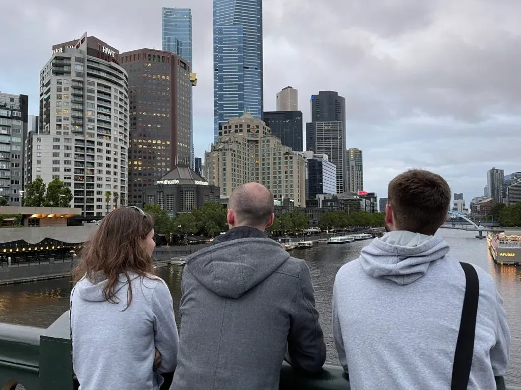 Three people from behind at a railing over the Yarra, Southbank and Eureka Tower beyond