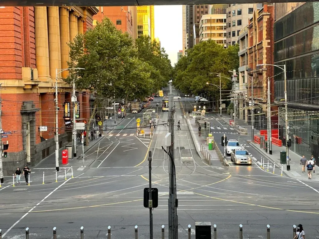 A near-empty intersection of tram tracks seen from above, red brick station building at left