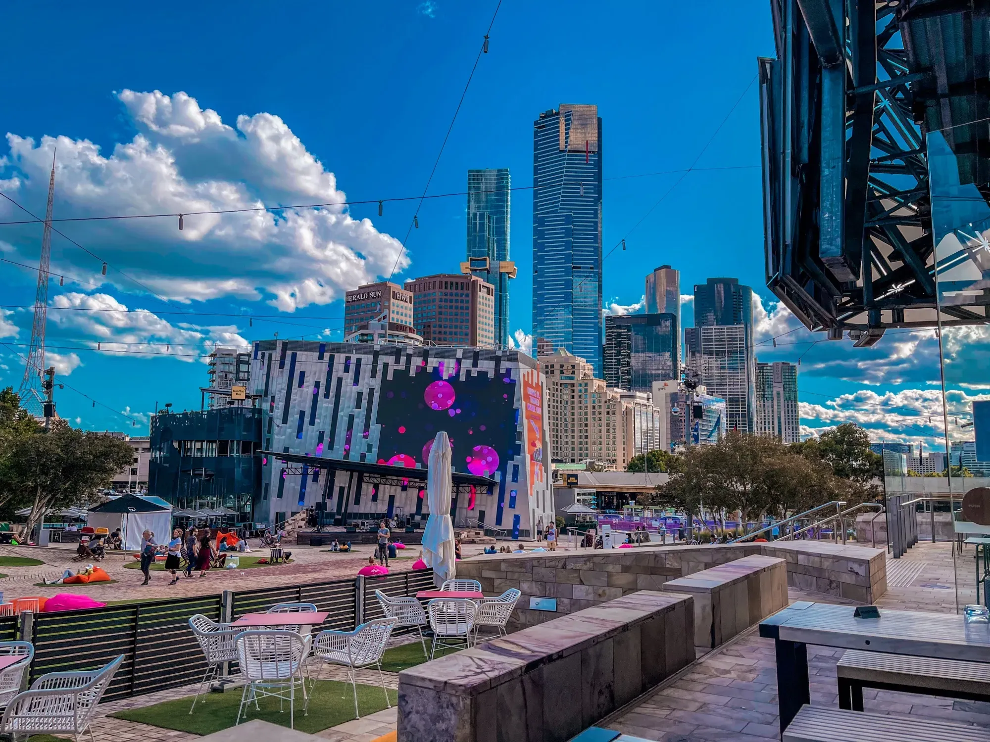 Federation Square big screen and deckchairs on a sunny afternoon, Eureka Tower and the Southbank skyline behind