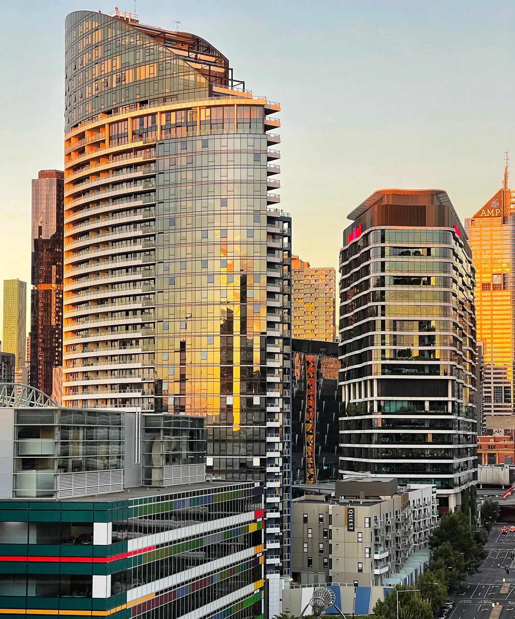 Curved glass apartment towers catching gold sunset light, the AMP building glowing behind them