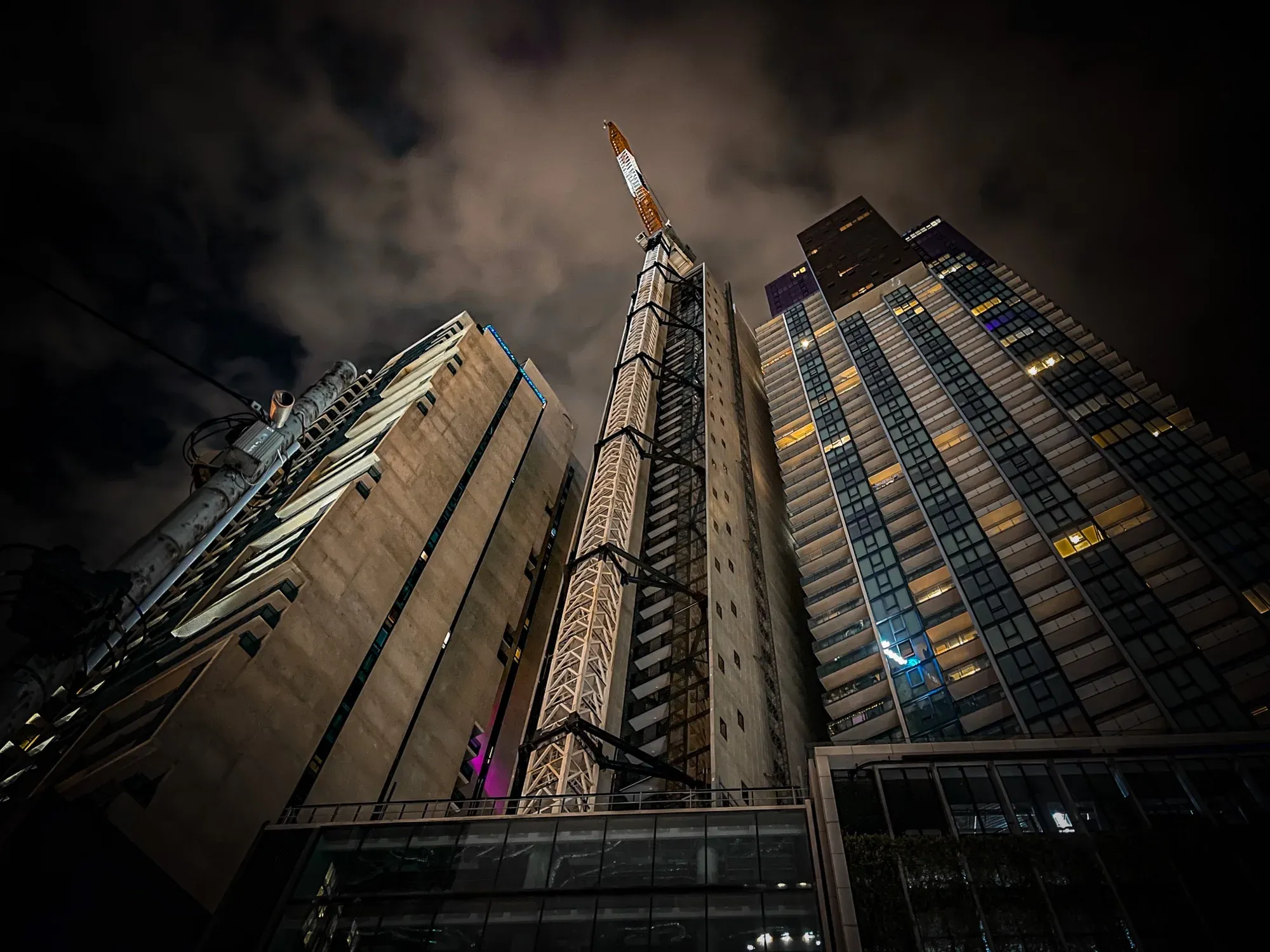 Looking up at apartment towers at night with a construction crane rising between them
