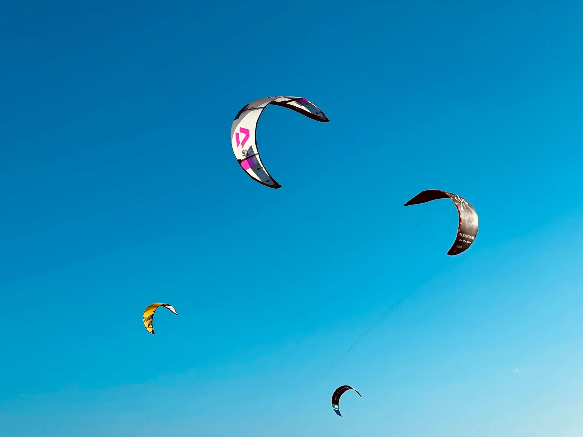 Four kitesurfing kites hanging at different heights against a clear blue sky
