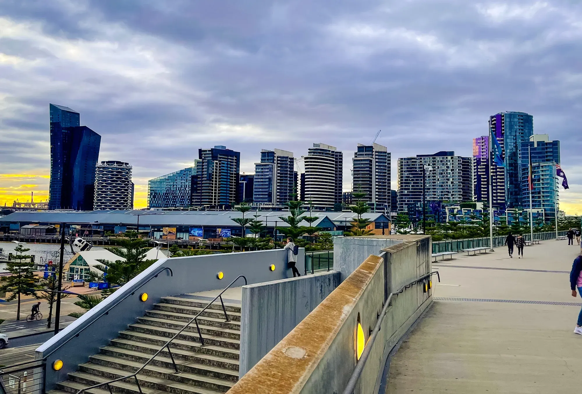 Docklands promenade steps studded with yellow lights at dusk, apartment towers and a sunset sky behind
