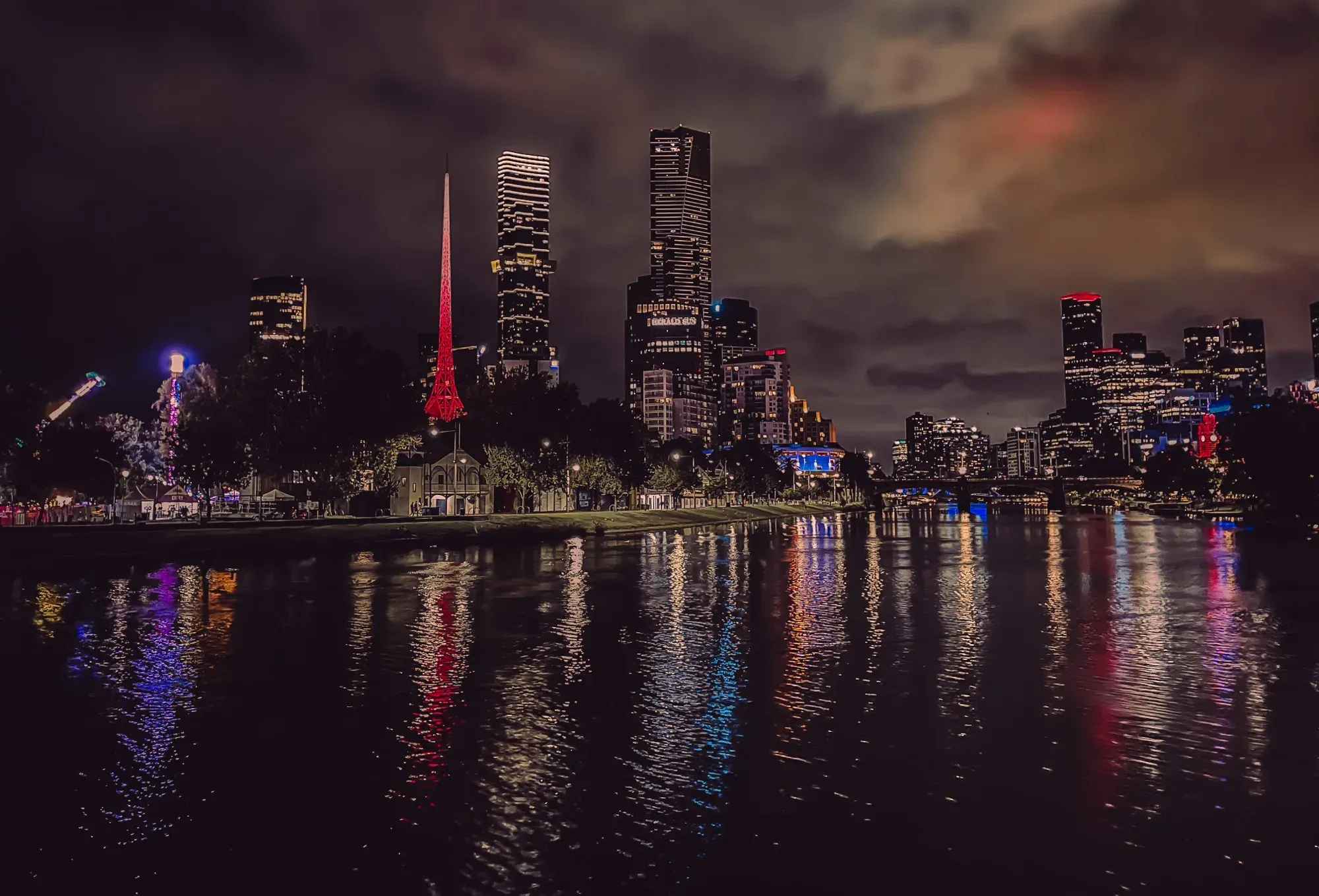 Arts Centre spire lit red above the night skyline, the lights stretched out across the Yarra