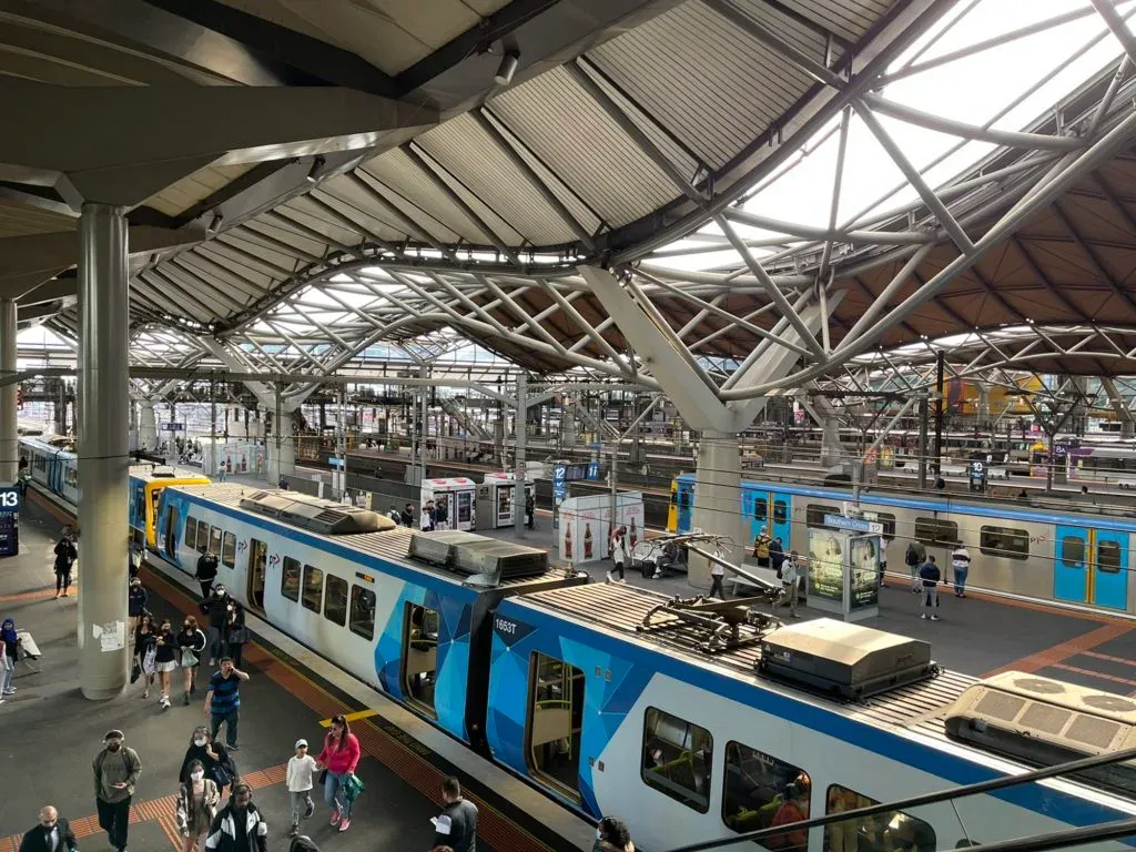 Trains at the platforms beneath the station's rippling steel roof, masked commuters walking below