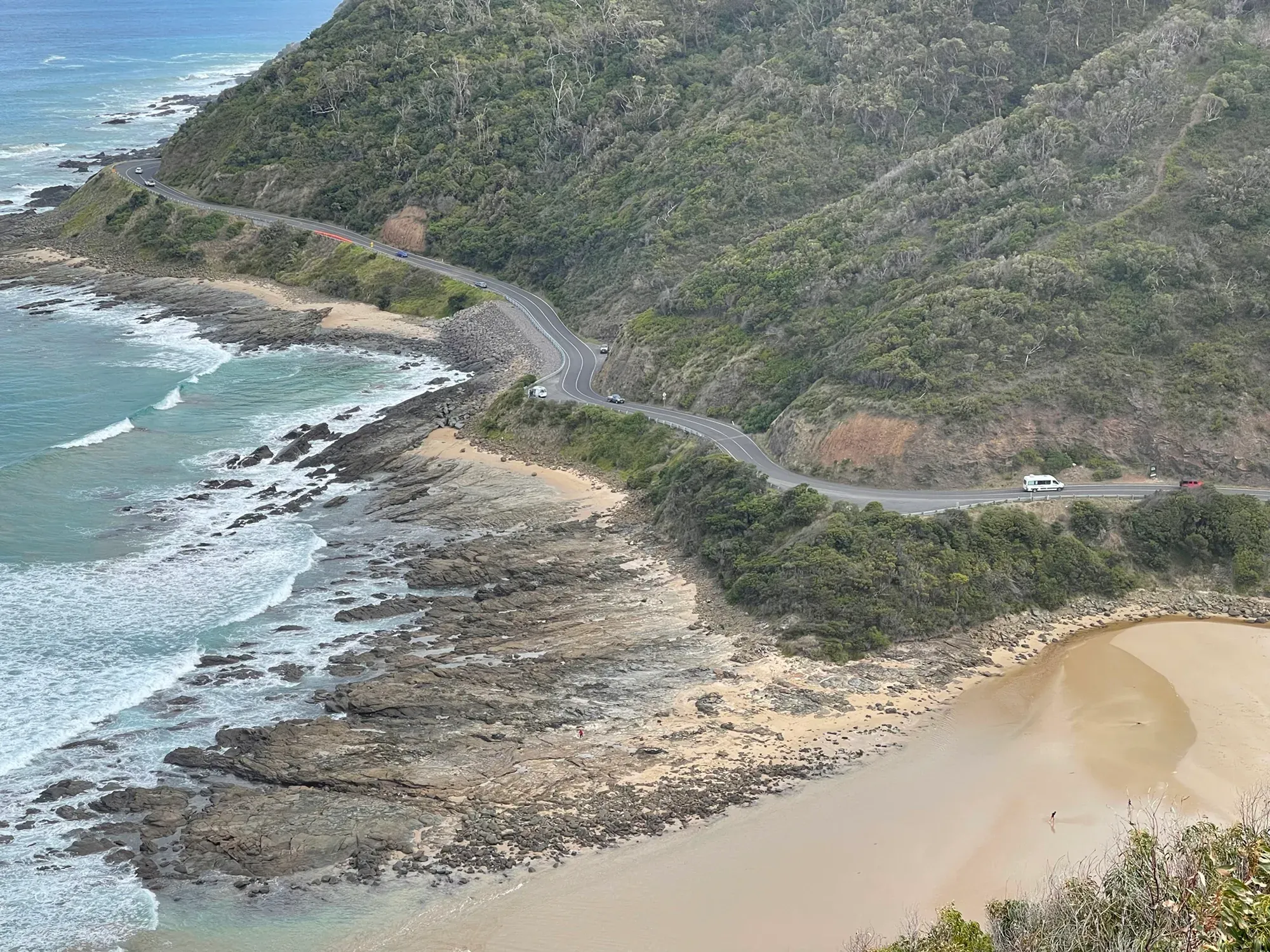 The road looping along the cliffs far below, a campervan and a few cars tiny on its bends