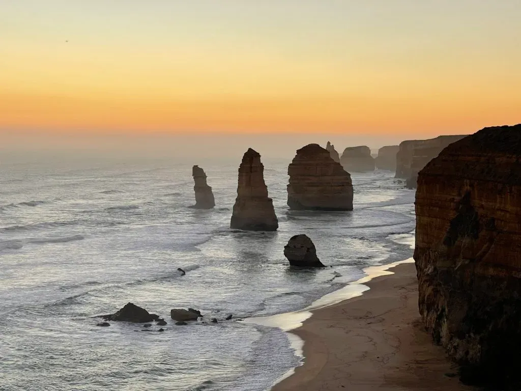 Limestone stacks standing in the shallows below the cliffs, orange sky after sundown