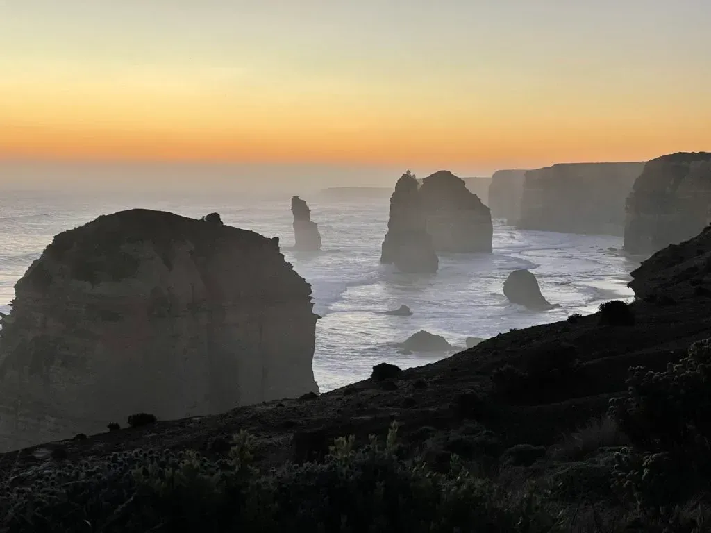 The stacks and headlands as dark silhouettes, pale surf and a fading orange horizon