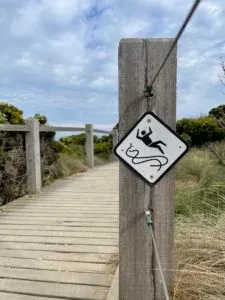 Black and white diamond sign on a boardwalk post, a figure tipping backwards over a wavy line