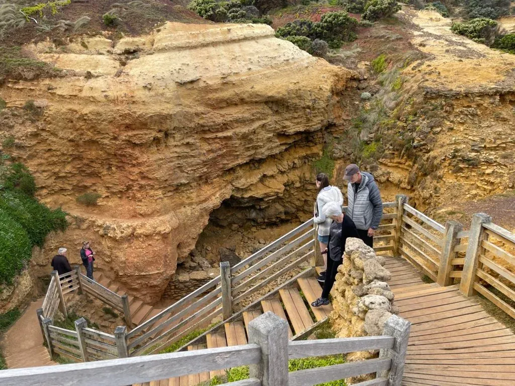 Visitors on switchback timber stairs descending into a layered ochre rock bowl