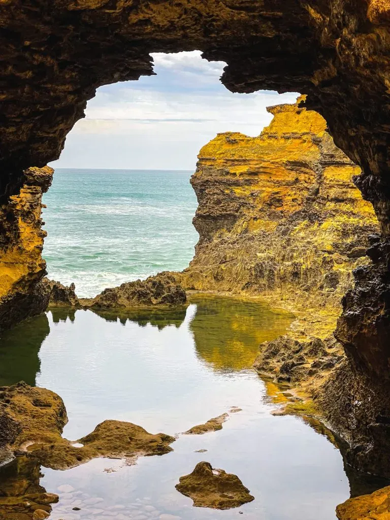 A rock window opening onto a mirror-still pool, with the open ocean breaking beyond it