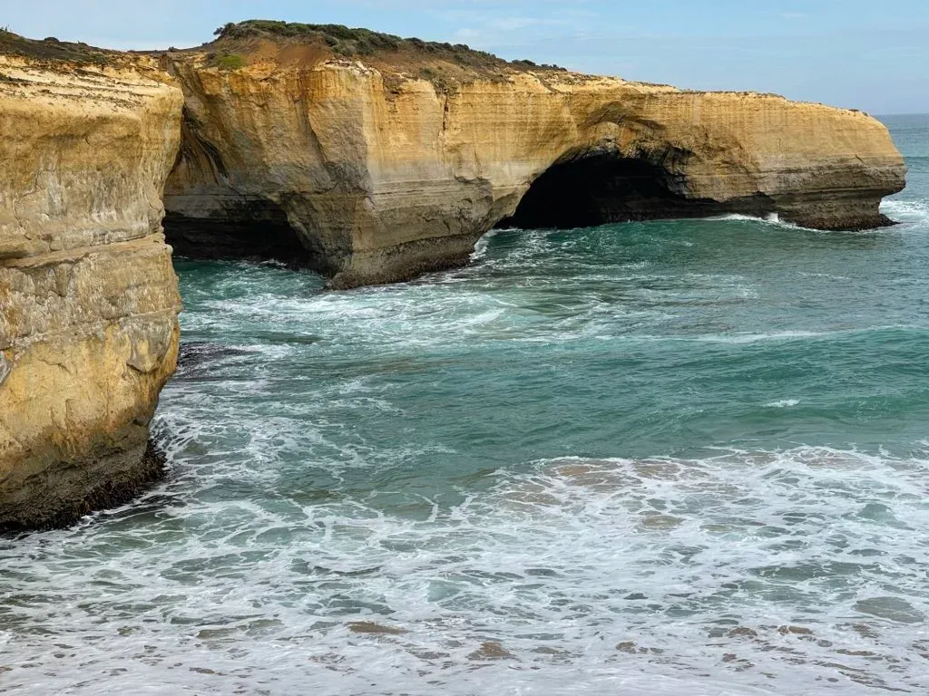 A dark sea cave cut into the foot of the cliff, turquoise water swirling at its mouth