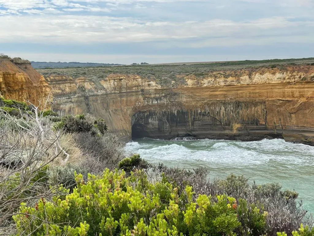 A streaked cliff wall with a cave at its foot, farmland running right to the edge above