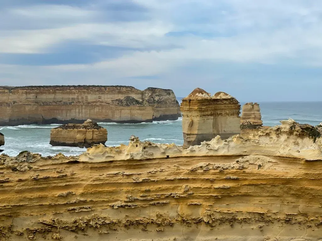 Wind-carved bands of ochre rock in the foreground, flat-topped stacks standing offshore