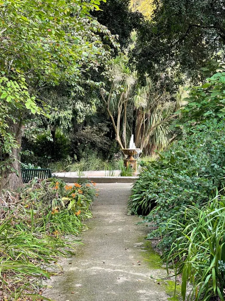A shaded gravel path through the gardens leading to a small tiered fountain