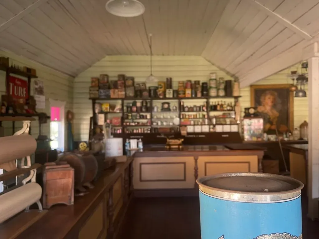 General store interior, shelves stacked with old tins and bottles behind a long timber counter