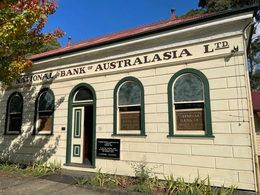 Cream stucco branch of the National Bank of Australasia Ltd, green arched windows and the door standing open