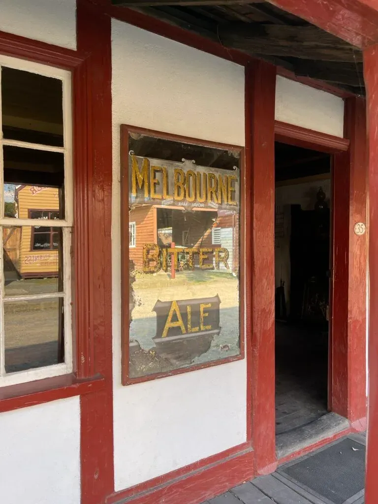 Peeling Melbourne Bitter Ale mirror beside an open doorway on a red-framed shopfront