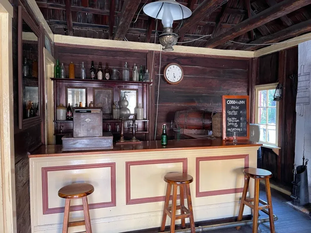 Timber bar with three stools, an old till and a chalked Cobb & Co Inn price list on the counter
