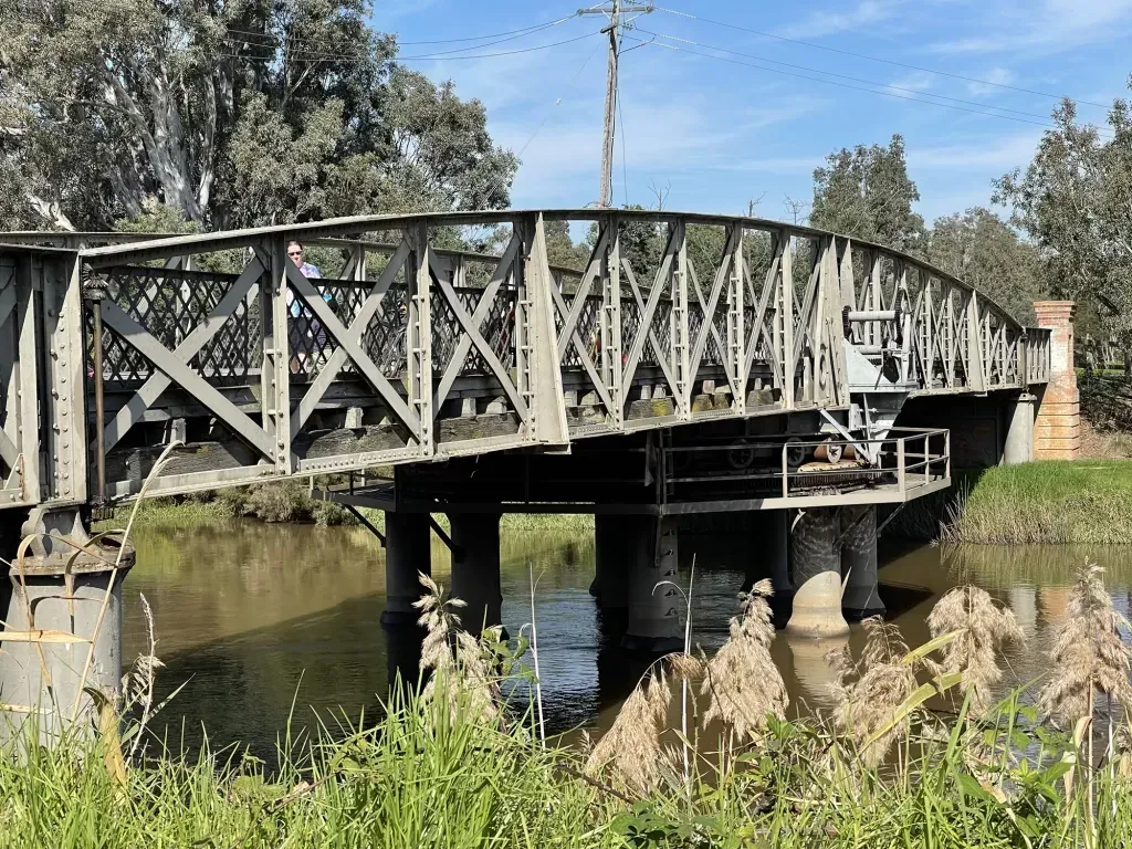 Side-on view of the bridge deck and its riveted lattice trusses, one person walking across