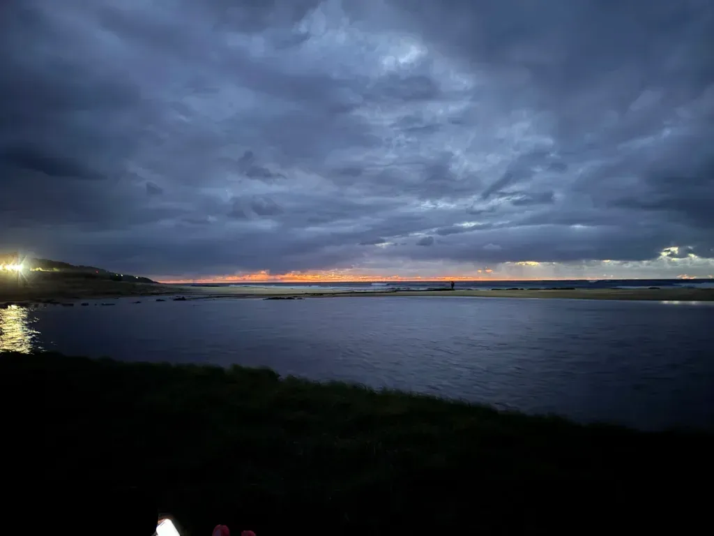 A thin orange band of sunrise under heavy cloud over the Southern Ocean, with a dark lagoon in front