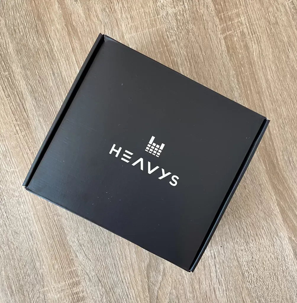 Closed matte black Heavys box with the white wordmark, on a pale wood floor