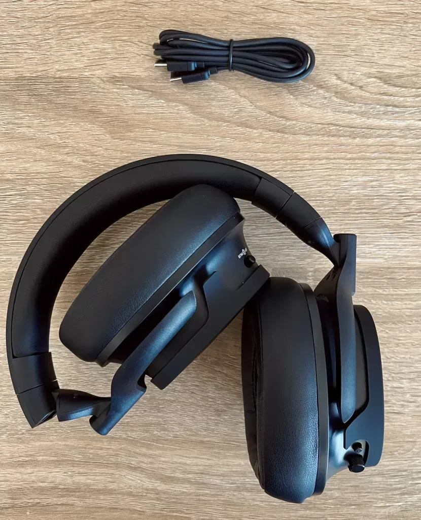 Headphones with one earcup swivelled flat, the short USB-C to USB-C cable coiled above them